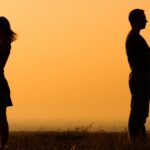 a couple facing away from each other in a field at sunset_s