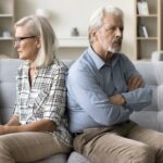 senior couple sitting on home couch back to back