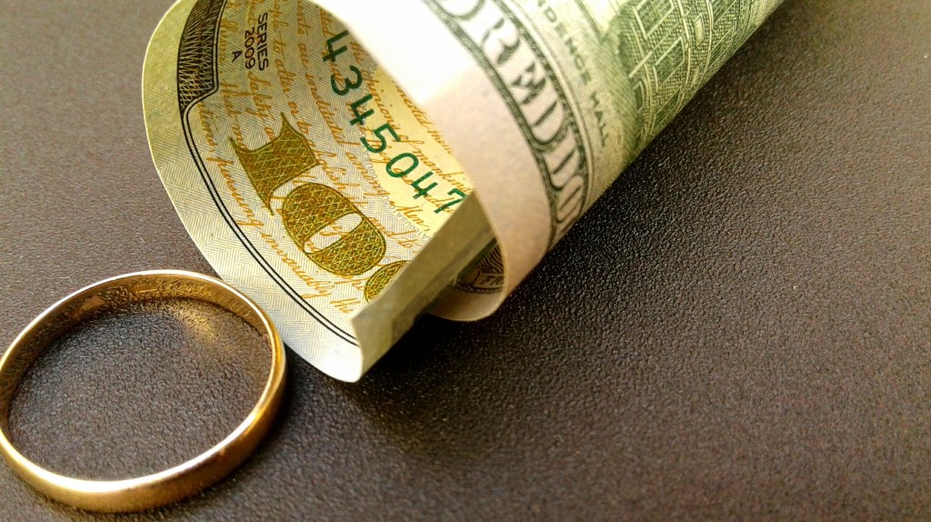 wedding ring lies next to 100 dollar bill